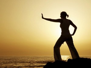 Yoga woman silhouetted against the setting sun with a natural reflection in a rockpool